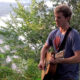 Ryan Howe playing acoustic guitar on the top of a bluff above the Mississippi River.